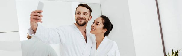 plan panoramique de l'homme joyeux prenant selfie tout en se tenant avec petite amie dans la salle de bain
  - Photo, image