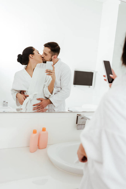 バスルームでボーイフレンドとキスしながら写真を撮る女性の選択的な焦点  - 写真・画像