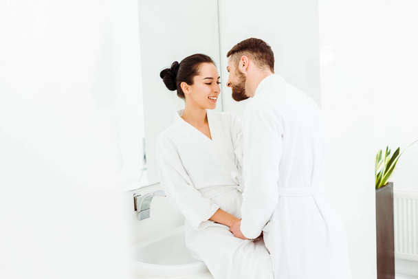selective focus of bearded man looking at happy brunette woman while holding hands in bathroom  - Photo, image
