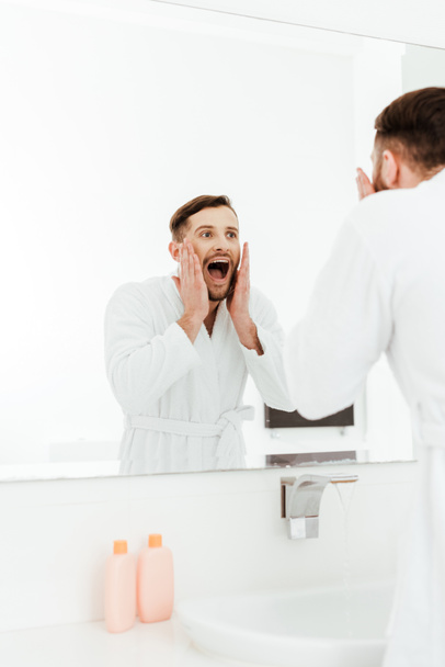 selective focus of handsome bearded man looking at mirror and screaming in bathroom  - Fotó, kép