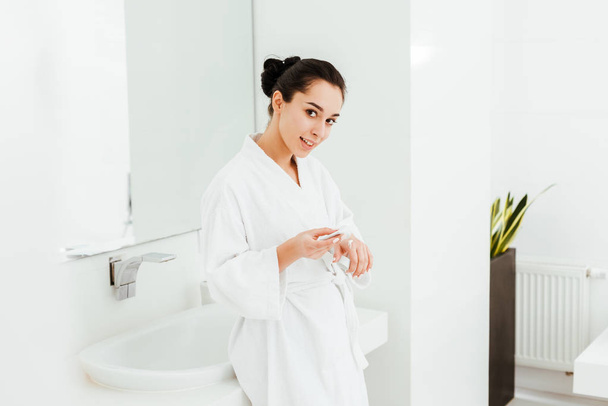 happy and attractive woman applying hand cream in bathroom  - Фото, изображение