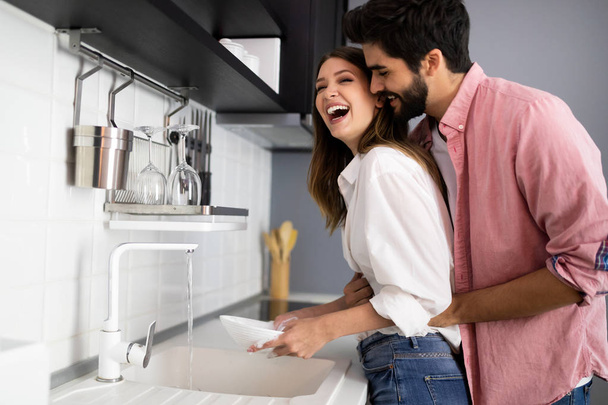 Young couple doing dishes in the kitchen while having fun and hugging - Φωτογραφία, εικόνα