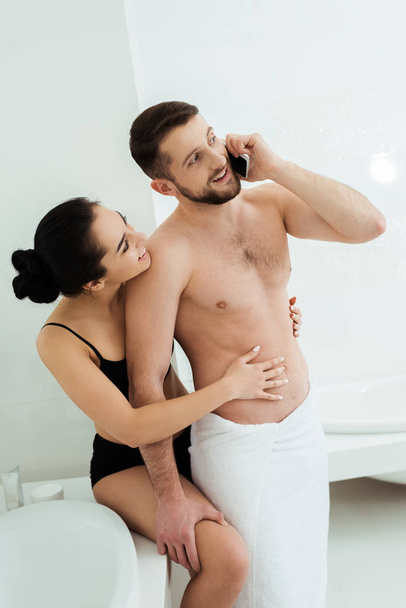 brunette woman in underwear looking at happy boyfriend talking on smartphone  - Photo, Image