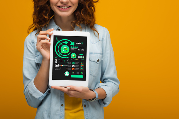 cropped view of curly girl holding digital tablet with charts and graphs isolated on orange  - Photo, Image