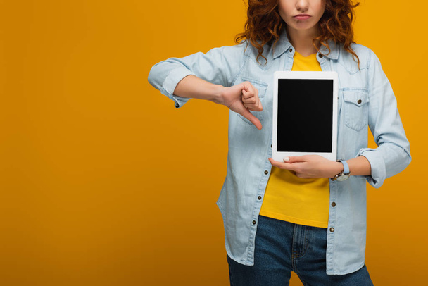 cropped view of upset curly woman holding digital tablet with blank screen and showing thumb down on orange  - Fotografie, Obrázek