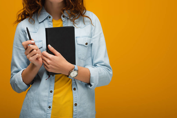 cropped view of young woman holding notebook and pen on orange  - Foto, Bild