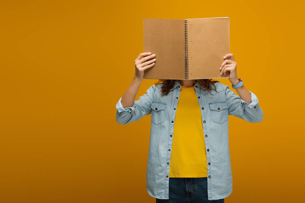 young woman standing and covering face with notebook on orange  - Фото, изображение