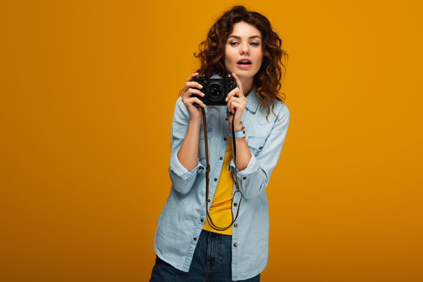 attractive redhead photographer holding digital camera on orange  - Fotó, kép
