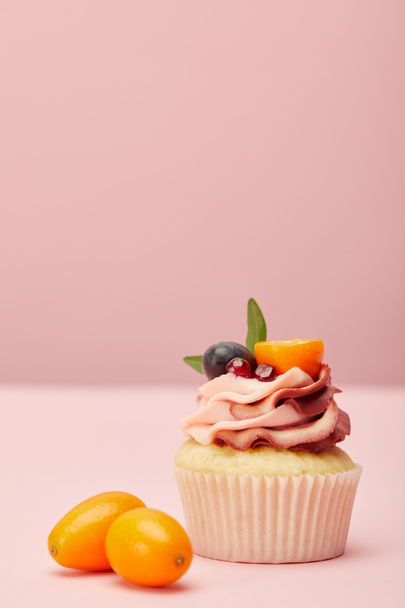 sweet cupcake with cream and two kumquats on pink surface - Фото, зображення