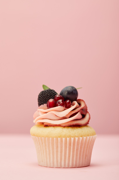 sweet cupcake with cream, berries and garnet on pink surface - Fotó, kép