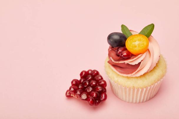 сладкий кекс со сливками и гранатом на розовой поверхности
 - Фото, изображение