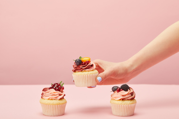 cropped view of woman with sweet cupcakes with fruits and berries isolated on pink - Foto, Bild