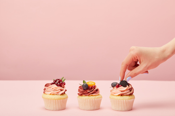 cropped view of woman with sweet cupcakes with fruits and berries isolated on pink - Фото, изображение