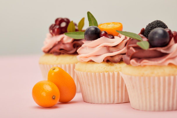 selective focus of cupcakes with kumquats on pink surface - Фото, зображення