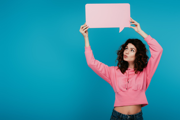 attractive curly girl with duck face holding pink speech bubble on blue  - Fotografie, Obrázek