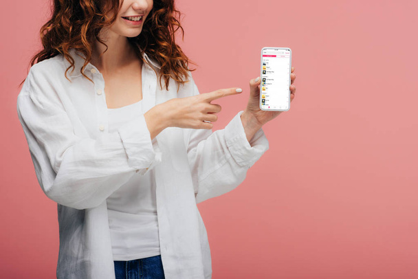 cropped view of cheerful girl pointing with finger at smartphone with apple music app screen on pink - Photo, Image