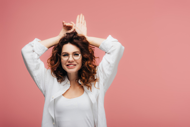 attractive curly woman in glasses smiling while gesturing on pink - Fotografie, Obrázek