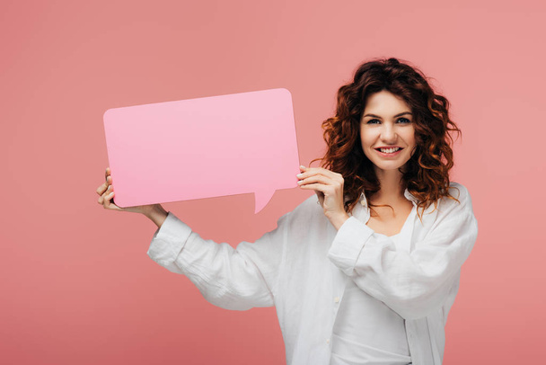 happy curly girl with red hair holding blank speech bubble on pink  - Foto, imagen