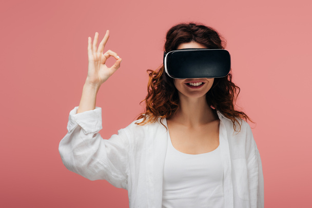 boldog göndör vöröshajú nő visel virtuális valóság headset és a bemutató ok jel-ra rózsaszín  - Fotó, kép