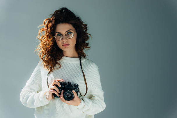 attractive young woman with red hair holding digital camera on grey  - Fotoğraf, Görsel