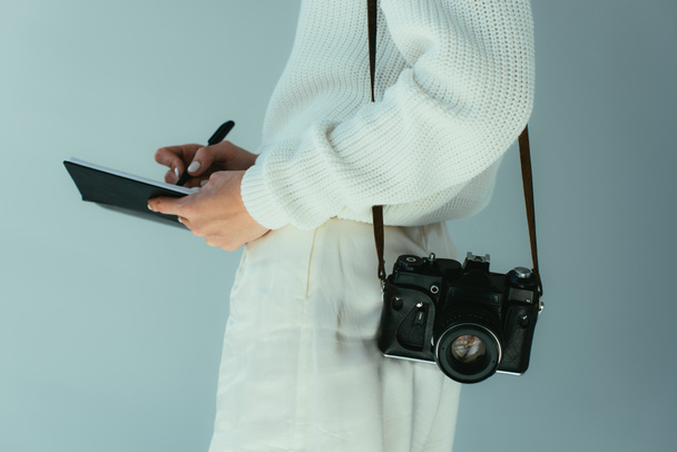 rajattu näkymä nuori nainen kirjoittaa muistikirjaan seisoessaan digitaalikamera harmaalla
  - Valokuva, kuva