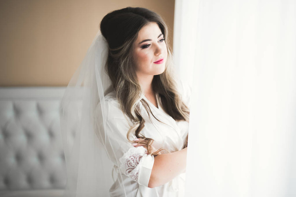 Splendida sposa in accappatoio in posa e preparazione per la cerimonia di nozze faccia in una stanza - Foto, immagini