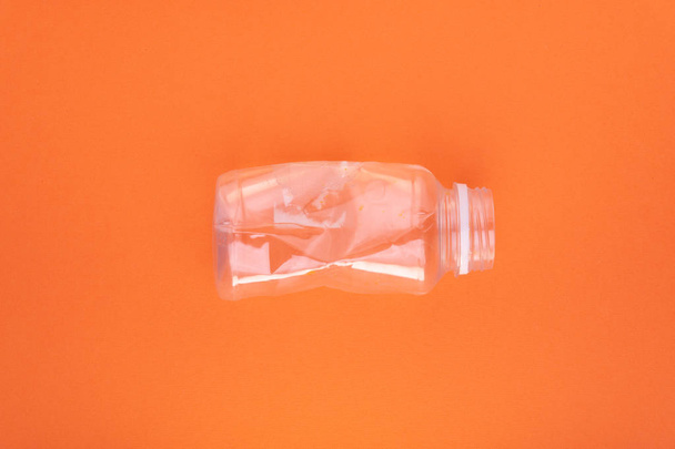 Разбитая пластиковая бутылка на оранжевом фоне. Концепция использования пластика. Экологическая проблема, глобальная окружающая среда
. - Фото, изображение