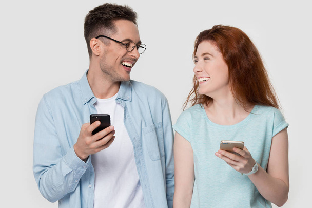 Smiling young couple holding smartphones laughing together - Valokuva, kuva