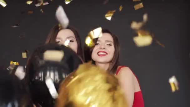 Beautiful twins in red and black dresses having fun with air balloons spraying with confetti. - Footage, Video