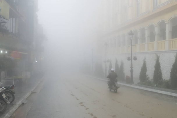 Мужчина едет на мотоцикле через густой туман в городе
. - Фото, изображение