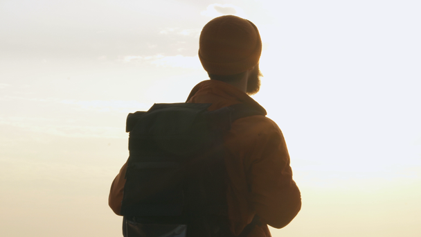 Backpacker op zoek naar de zonsondergang in de buurt van de zee. Uitzicht vanaf achterzijde. - Video