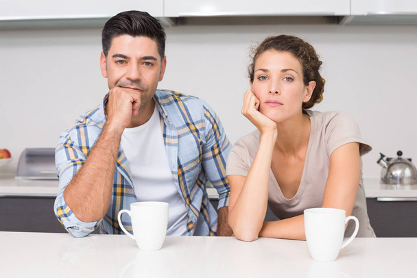 Fed up couple having coffee looking at camera at home in kitchen - Фото, зображення
