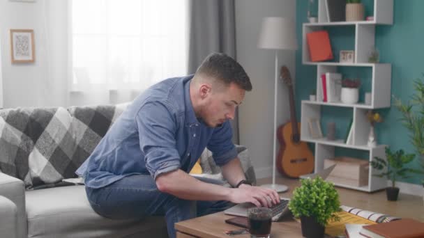 Young man with laptop computer calling on smartphone at home - Filmmaterial, Video