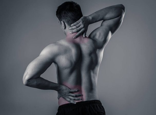 Young muscular fitness man touching and grabbing his neck and lower back suffering cervical pain isolated on neutral background. In sport and workout injury, Incorrect posture problems and body care. - Fotó, kép