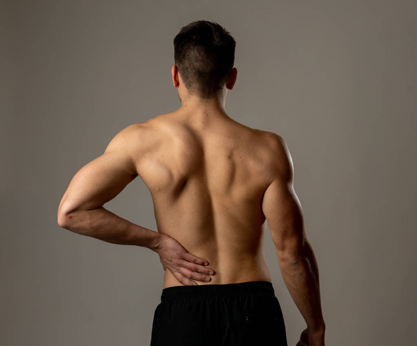 Young muscular fitness man touching and grabbing his lower back suffering strong pain after workout. Isolated on neutral background. In sport injury Incorrect posture problems and body health care. - Фото, зображення