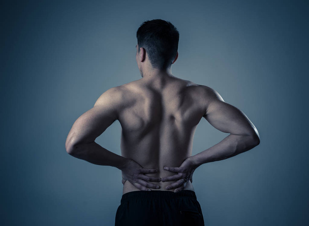 若い筋肉のフィットネスの男は、トレーニング後に強い痛みに苦しんで彼の腰をつかんでつかみます。ニュートラルな背景で隔離されています。スポーツ傷害不適切な姿勢の問題と体の健康管理. - 写真・画像