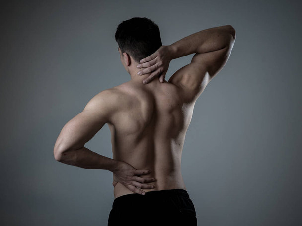 Young muscular fitness man touching and grabbing his neck and lower back suffering cervical pain isolated on neutral background. In sport and workout injury, Incorrect posture problems and body care. - Fotografie, Obrázek