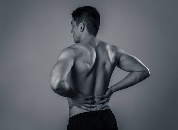 Young muscular fitness man touching and grabbing his lower back suffering strong pain after workout. Isolated on neutral background. In sport injury Incorrect posture problems and body health care. - Photo, image