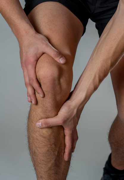 Young fit man holding knee with hands in pain after suffering muscle injury broken bone leg pain sprain or cramp during running workout. In Body pain and sport training injury and body health care. - Photo, Image