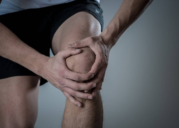 Young fit man holding knee with hands in pain after suffering muscle injury broken bone leg pain sprain or cramp during running workout. In Body pain and sport training injury and body health care. - Photo, image