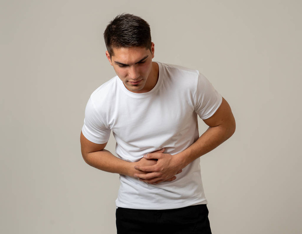Young muscular fitness man holding his stomach suffering strong abdominal pain. Isolated on neutral background. In stomachache, digestive problems and health care issues. - Valokuva, kuva