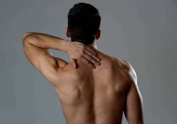 Молодой мускулистый мужчина прикасается к шее и верхней части спины, страдая от боли в шейке после тренировки. Изолирован на нейтральном фоне. При спортивной травме неправильная осанка и здоровье тела
. - Фото, изображение
