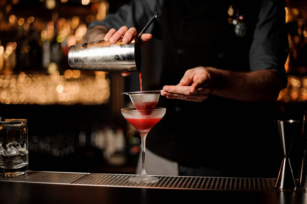 Bartender uses shaker and sieve to make cocktail - Foto, Bild