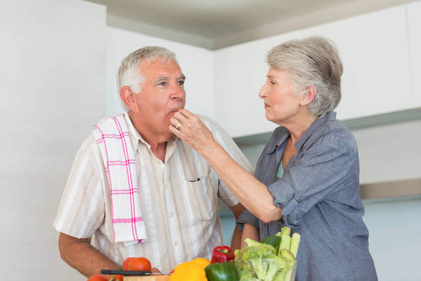 Happy senior couple preparing vegetables at home in the kitchen - Фото, изображение