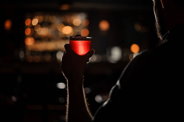 Darkened shot of bartender with red alcohol cocktail - Фото, изображение