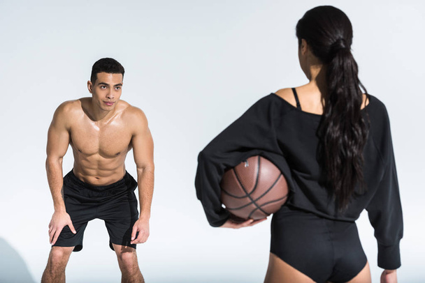 handsome mixed race man looking at sportive african american woman with ball on white - Photo, Image