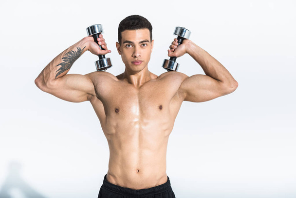 handsome mixed race athletic man with muscular torso holding dumbbells on white - Photo, image