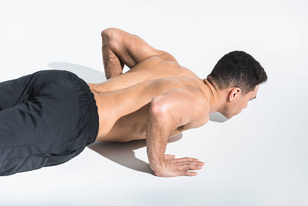 athletic shirtless mixed race man doing push ups on white - Fotó, kép
