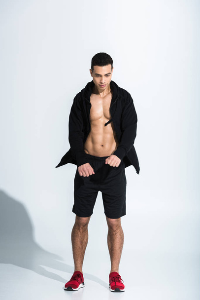 handsome mixed race man in black sportswear and red sneakers warming up on white - 写真・画像