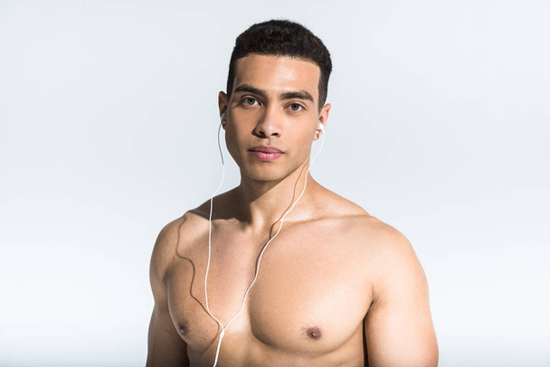 handsome athletic man with muscular torso listening music in earphones on white - 写真・画像